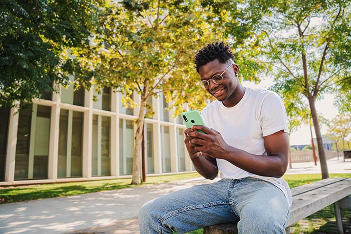 Student_720x480 College student using his mobile phone sitting on a bench on a college campus